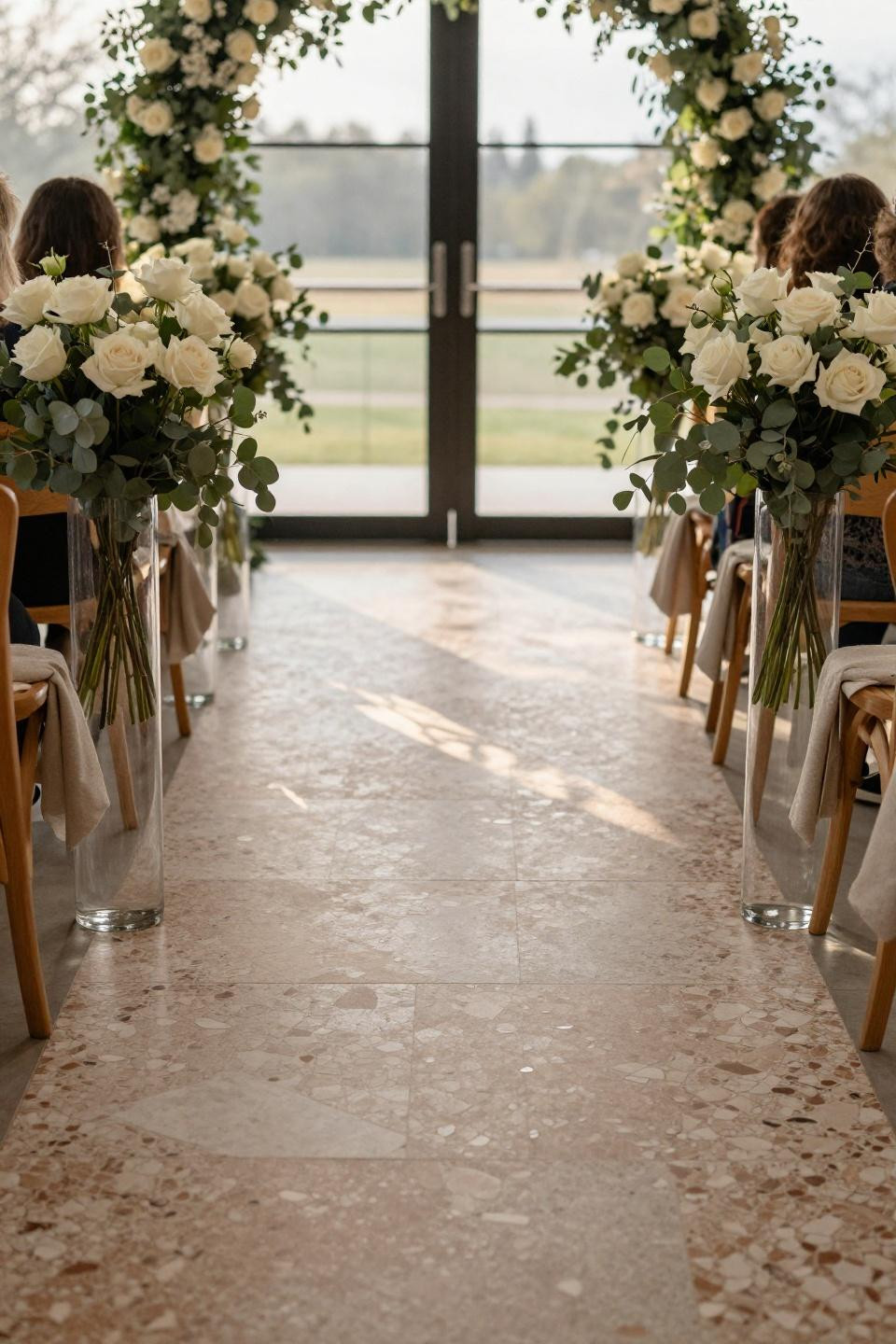 Outdoor wedding aisle ideas featuring custom terrazzo and glass vessels with roses
