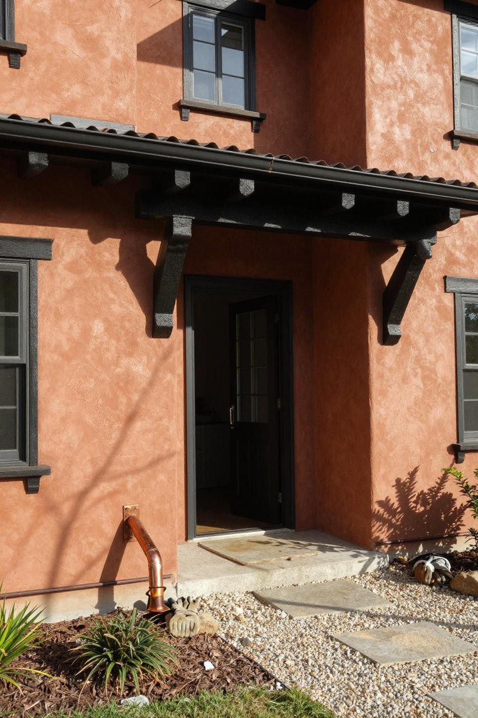 Warm terracotta stucco ranch mansion exterior with black timber beams and metal carport