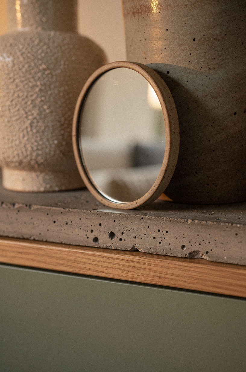 Nest a small oval mirror against stoneware (The Quiet Reflection Move)